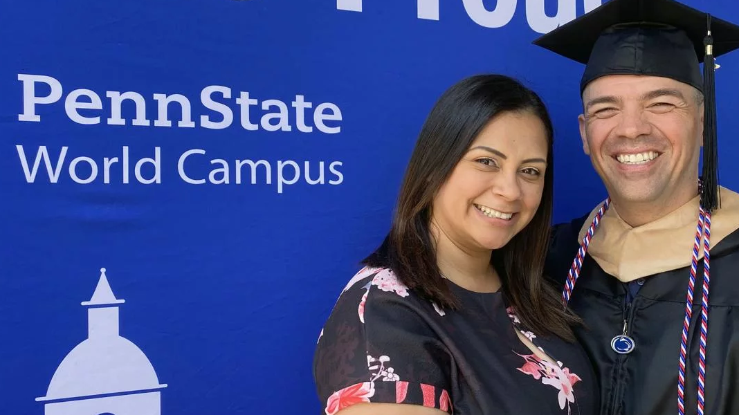 Penn State World Campus graduate poses in cap and gown with his partner