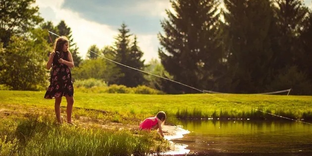 Woman fishing in a pond with child nearby.